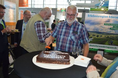 Gerhard Hesse schneidet die Jubiläumstorte für 15 Jahre Qualitätszertifizierung Eggeweg auf der Messe Tour Natur in Düsseldorf an.